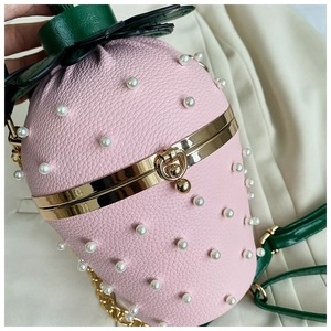 Detail of pink strawberry bag with white pearls, leather texture, and green leaf clasp