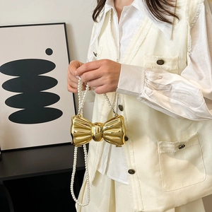 Chic gold bow-shaped metal clutch with pearl chain strap worn by a woman for evening