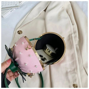 Detail of strawberry cross-body bag featuring pink leather, pearls and green leaf decor