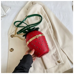 Macro detail of strawberry-shaped crossbody bag with gold hardware and leaf lid