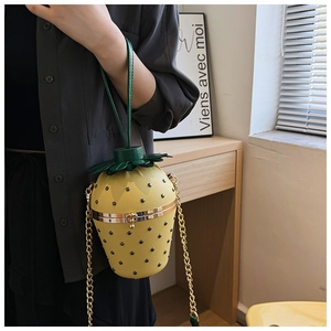 Detail of strawberry-shaped crossbody bag with gold chain and green leather handle