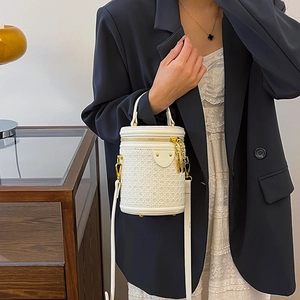 White woven cylinder bucket bag with gold hardware worn by a model in a modern interior