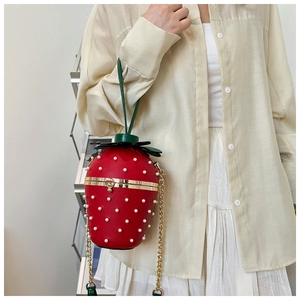 Detail of red strawberry handbag with pearl studs and golden chain on model