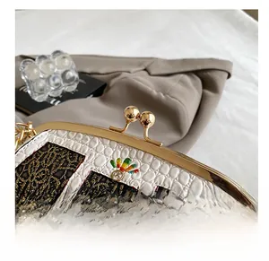 Close-up of white crocodile pattern and black lace trim with gold kiss-lock closure