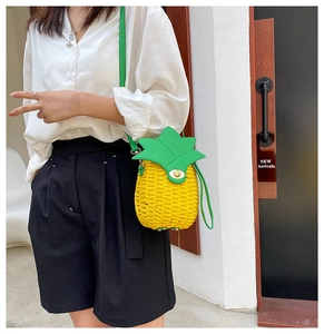 Close-up of pineapple-shaped woven straw crossbody bag with green leaf lid and gold buckle
