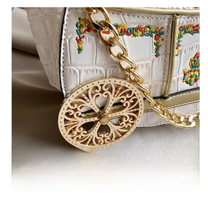 Close-up of white croc-embossed bag with floral embroidery and gold chain details