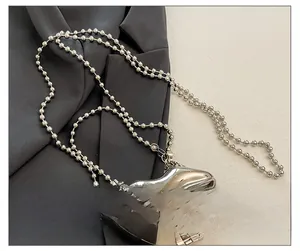 Detail of silver lip-shaped metal clutch bag with bead chain strap on grey fabric