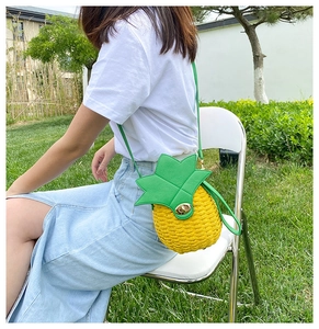 Detail view of handmade straw crossbody bag in yellow pineapple shape with green leaf flap