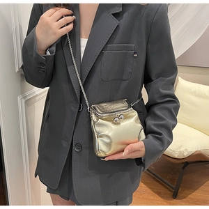 Detail of a mini gold crossbody bag with chain strap shown on a dark blazer