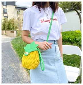 Detail of a pineapple shaped woven bag with green leaf decor and a slim strap