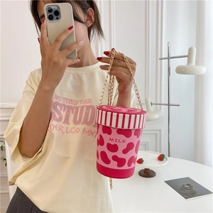 Pink strawberry milk bucket bag with cow print and gold chain strap in a lifestyle setting