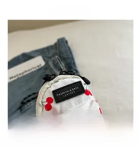 Detail of white canvas mini bag with red cherry prints and black leather fashion label