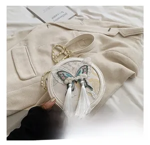 Détail d'un sac bandoulière rond blanc avec broderie papillon et pompons en perles