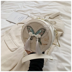 Détail de la broderie papillon et nœud en perles avec glands sur un sac rond blanc cassé