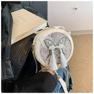 Détail du sac rond blanc avec broderie papillon, perles et élégants longs pompons