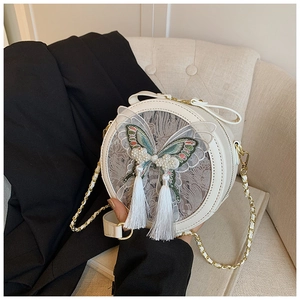 Détail du sac bandoulière rond beige avec broderie papillon, perles et glands