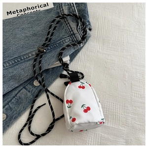 Detailed close-up of a mini cherry print crossbody bag with woven strap on denim background