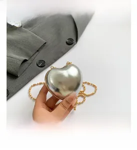 Detail of silver heart-shaped bag with gold bead chain over grey blazer jacket