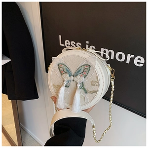 Détail du sac rond blanc avec broderie papillon vert, pompon et perles décoratives