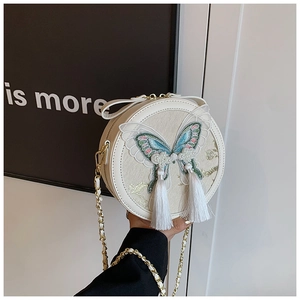 Détail du sac bandoulière rond blanc avec broderie papillon bleue et longues franges