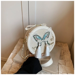 Détail du sac rond blanc avec broderie papillon, sequins brillants et pompons en soie