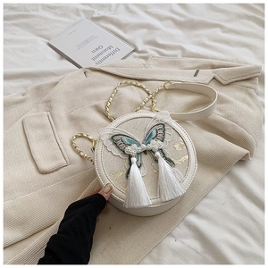 Détail du sac à bandoulière rond blanc avec broderie papillon et deux pendentifs pompons
