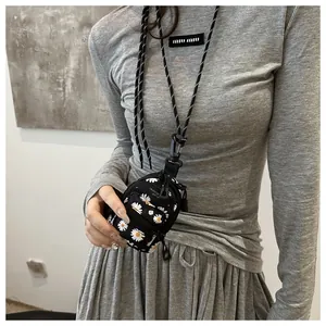 Detail of mini black crossbody bag with white daisy print and braided neck strap