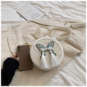 Détail du sac rond blanc avec broderie papillon bleue et pompons en perles élégants