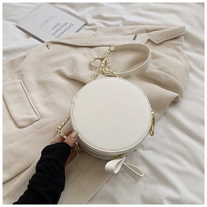 Détail du sac rond blanc avec nœud décoratif et chaîne dorée sur fond de textile doux