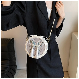 Détail du sac rond blanc avec broderie papillon, perles élégantes et glands en soie