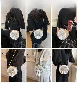 Détail du sac à bandoulière rond avec broderie papillon et pompons blancs