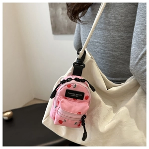 Detail view of mini pink cherry print backpack charm attached to a white shoulder bag