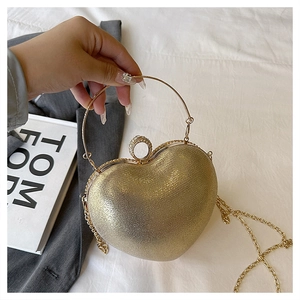 Detail of a gold heart-shaped evening clutch bag with chain strap and round metal handle