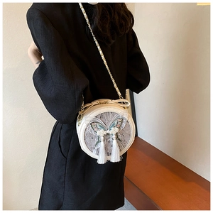 Sac bandoulière rond blanc avec broderie papillon et pompons porté par mannequin