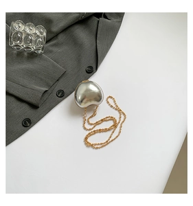 Detail shot of silver heart-shaped mini bag with golden beaded chain on a white table