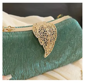 Detailed view of dark green evening bag with glitter texture and gold leaf metal clasp