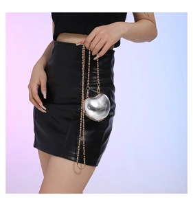 Detail of silver heart-shaped mini crossbody bag with gold ball chain on model