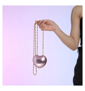 Macro shot of metallic pink heart-shaped mini bag with gold bead chain and mirror finish