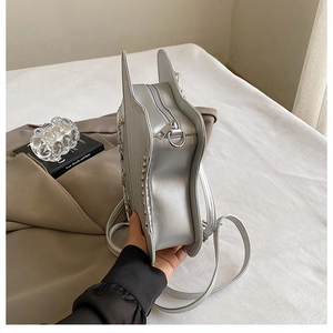 Close-up of silver piano-shaped shoulder bag featuring metal studs and unique side wing design