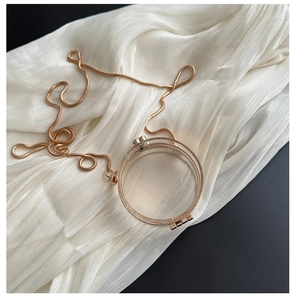 Detail of round transparent acrylic mini bag with gold metal frame on white silk fabric