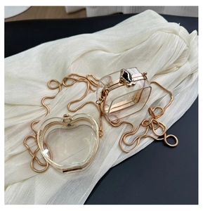 Detail of mini clear acrylic bags with gold frames and snake chain on white fabric