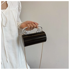 Detail of a black cylindrical acrylic evening bag with silver twin lion head handles and chain