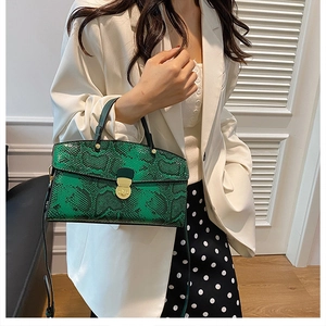 Green snakeskin tote bag with gold clasp shown on a model in a stylish white outfit