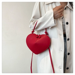 Detail of red heart-shaped leather crossbody bag with dual zippers and slender strap