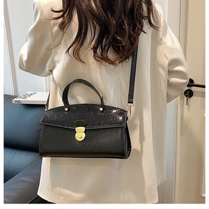 Detail of black faux leather tote with crocodile pattern and golden metal buckle