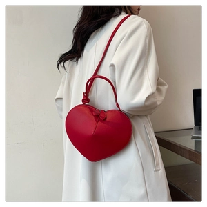 Macro view of a red heart-shaped leather crossbody bag with dual zipper and top handle