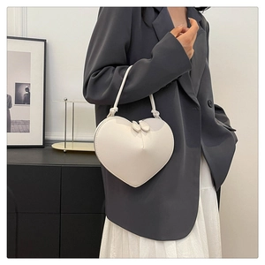 Detail of a white heart-shaped handbag featuring dual leaf-motif zippers and a top handle
