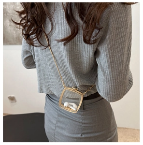 Close-up of a mini transparent acrylic crossbody bag with a gold metal chain strap