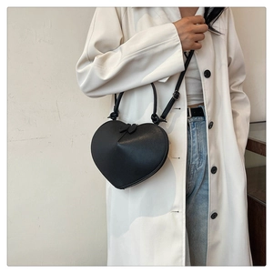 Close-up of heart-shaped crossbody bag with smooth leather finish and double zipper details