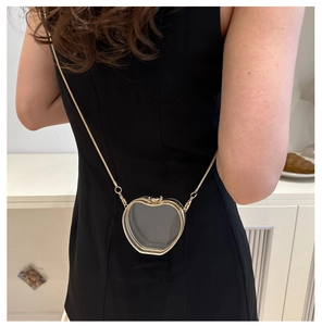 Detail of apple-shaped transparent acrylic mini bag with gold chain strap on shoulder